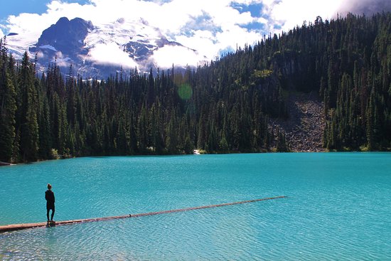 A woman stands on a log in a glacier lake in the mountains